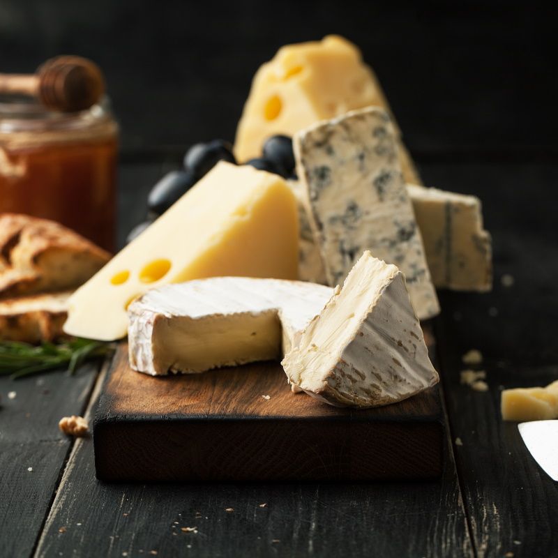Assorted Cheeses With Grapes, Nuts And Rosemary On A Wooden Background
