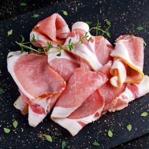 Raw Smoked Bacon Slices On Black Stone Board Which Herbs.