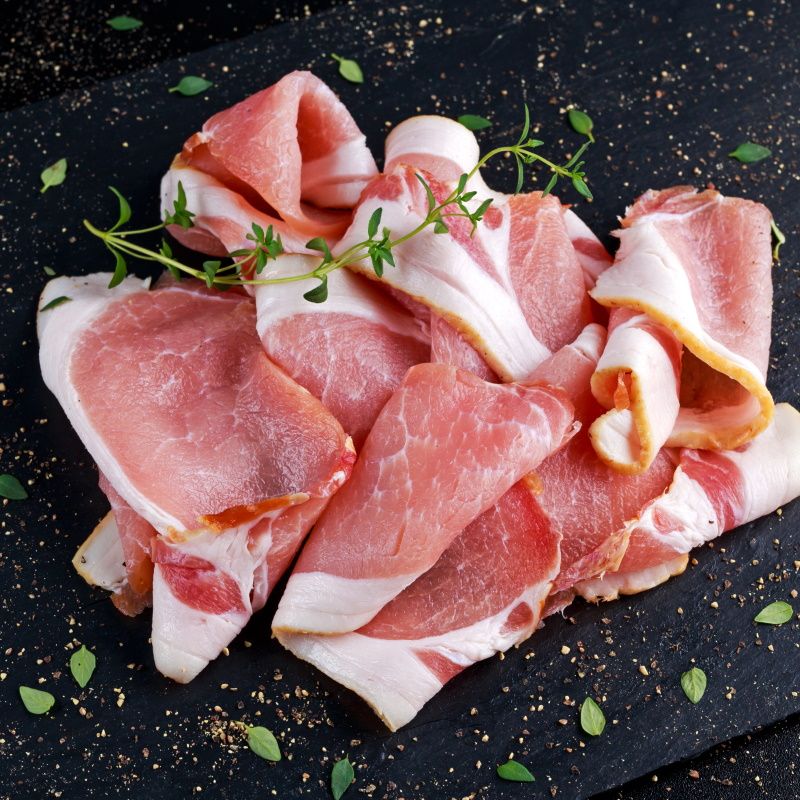 Raw Smoked Bacon Slices On Black Stone Board Which Herbs.