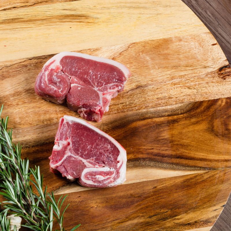Raw Lamb Loin Slices On Chopping Board With Herbs