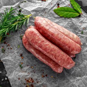 Freshly Made Raw Breed Butchers Sausages In Skins With Herbs On Crumpled Paper