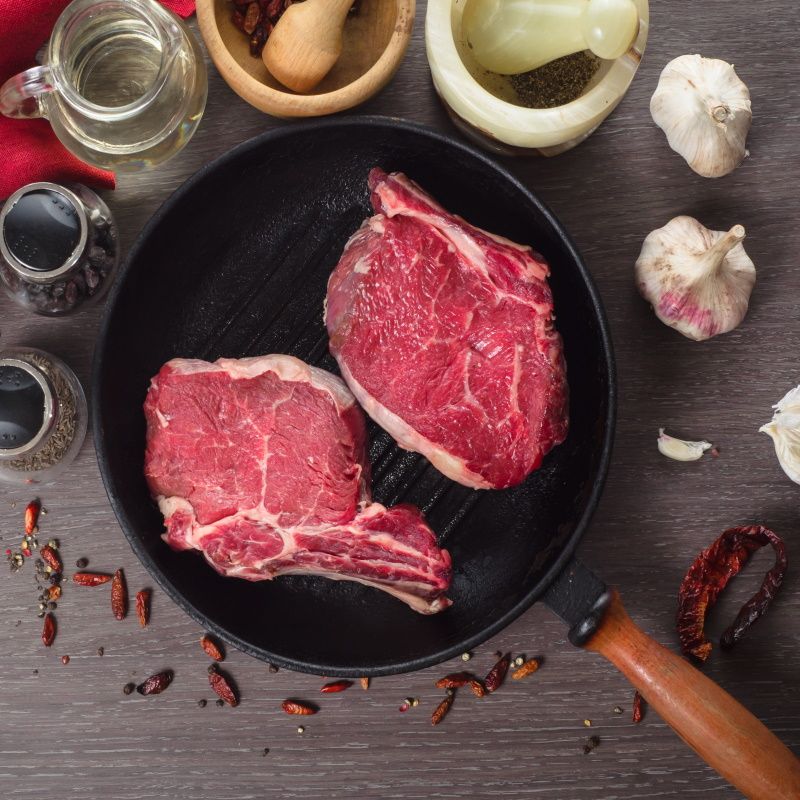 Raw Fresh Meat Rib Eye Steak Composition In Grill Pan On A Wooden Background